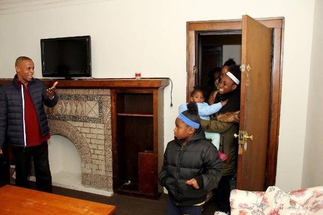 Man gesturing to group in a living room with fireplace and TV.
