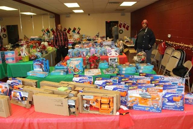 People stand behind tables filled with Christmas toys.
