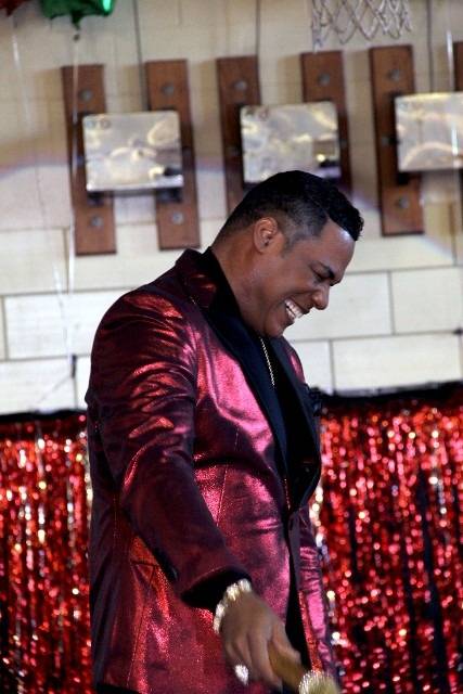 Man in a red sparkly suit smiling and holding a microphone