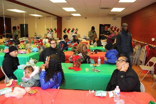 A holiday event with people gathered around tables decorated with gifts and Christmas decorations.