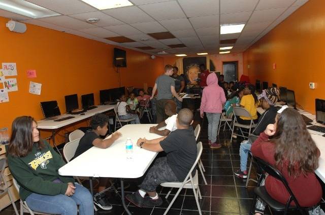 Children at a computer lab with vibrant orange walls.