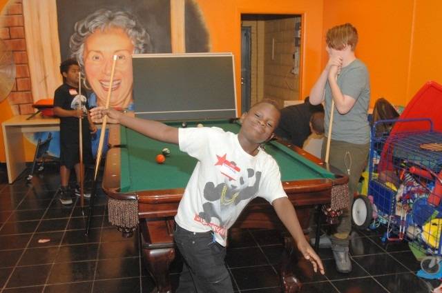 Young boy poses with pool cue by pool table