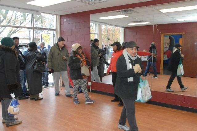 People line up at an event, some carry groceries.