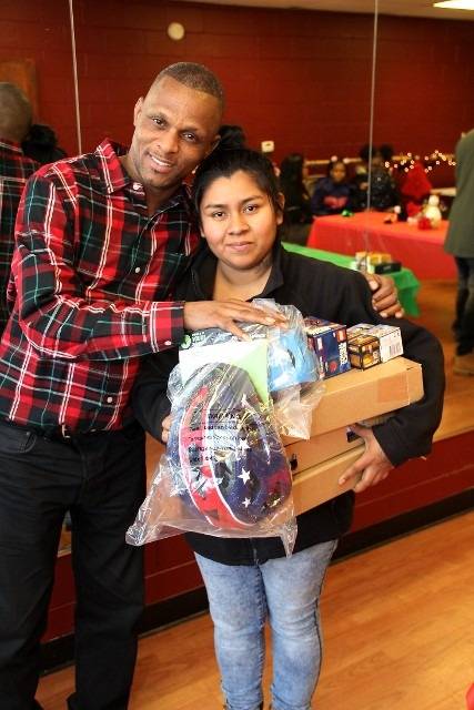 Two smiling people pose for a photo, one holding presents.