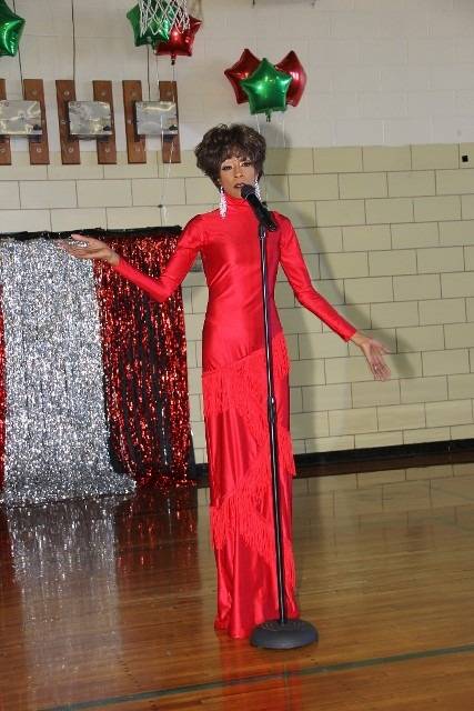 A performer in a red dress and wig on stage.