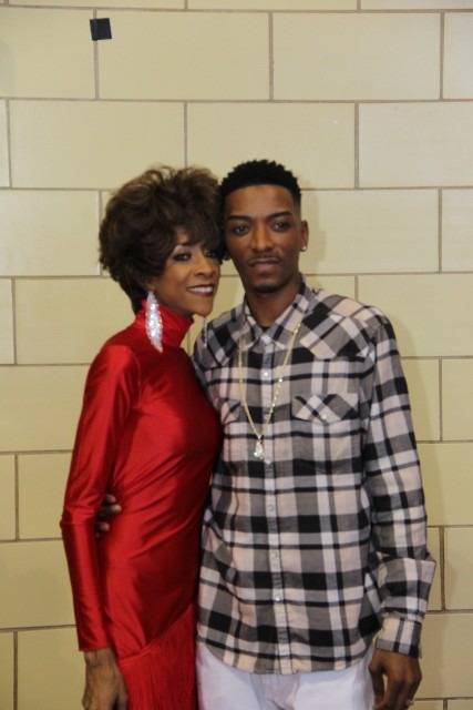 Two people smiling, posing in front of a brick wall.